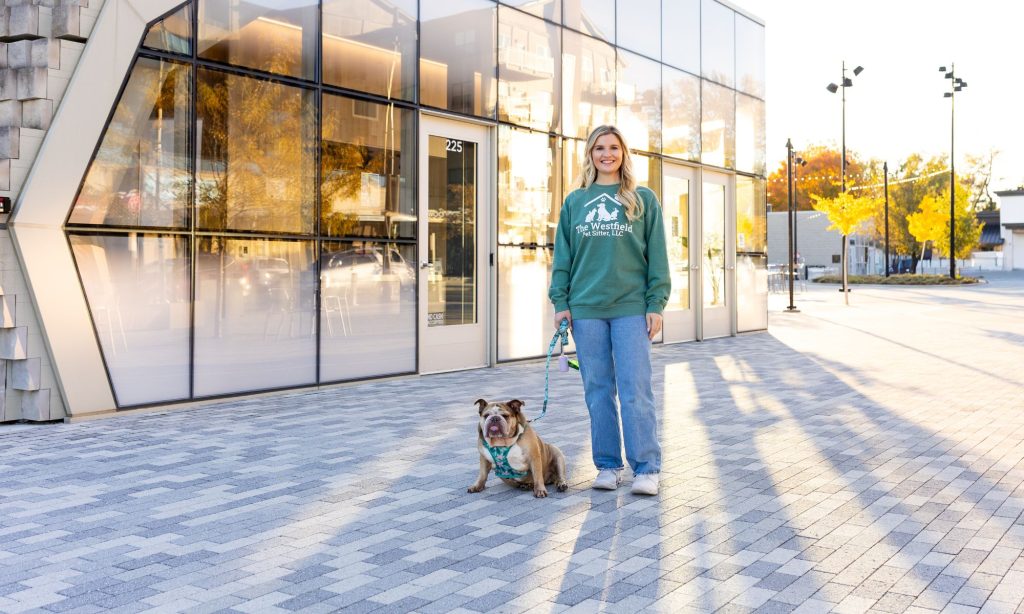 Woman with bulldog standing outside Westfield Pet Sitter office in daylight.