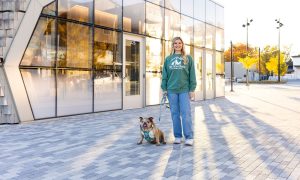 Woman with bulldog standing outside Westfield Pet Sitter office in daylight.