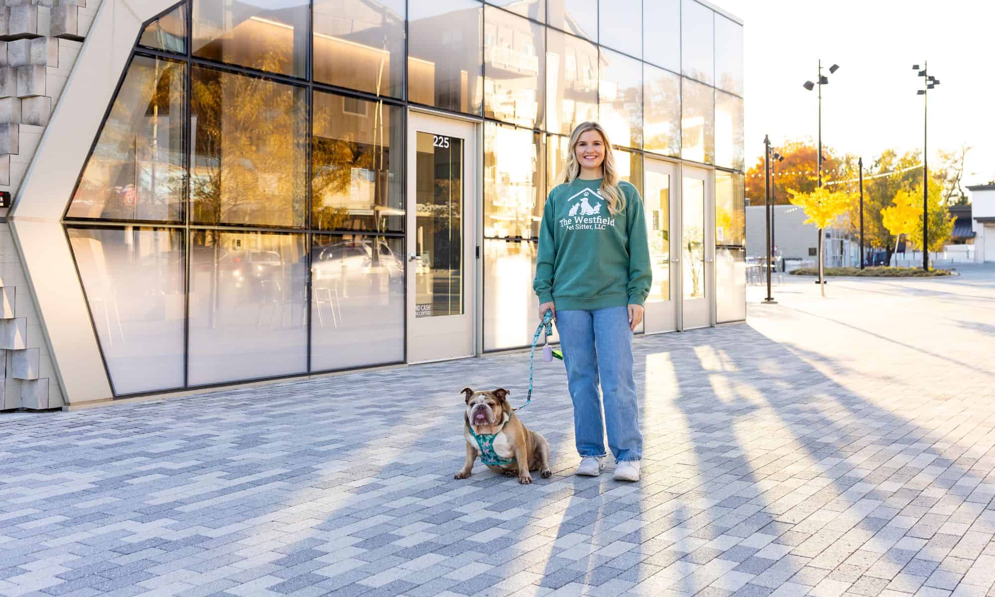 Woman with bulldog standing outside Westfield Pet Sitter office in daylight.
