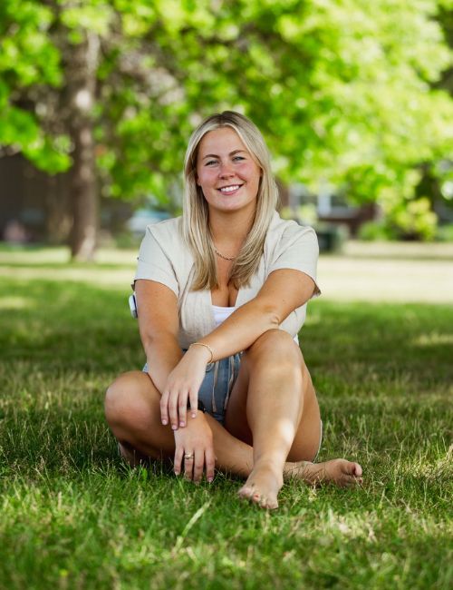 Grace, a pet sitter and dog walker in Westfield, sitting and smiling outdoors in a park